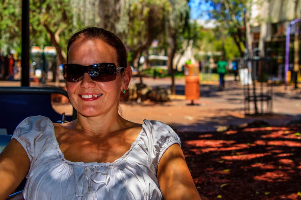 Frau mit Sonnenbrille sitzend im Schatten